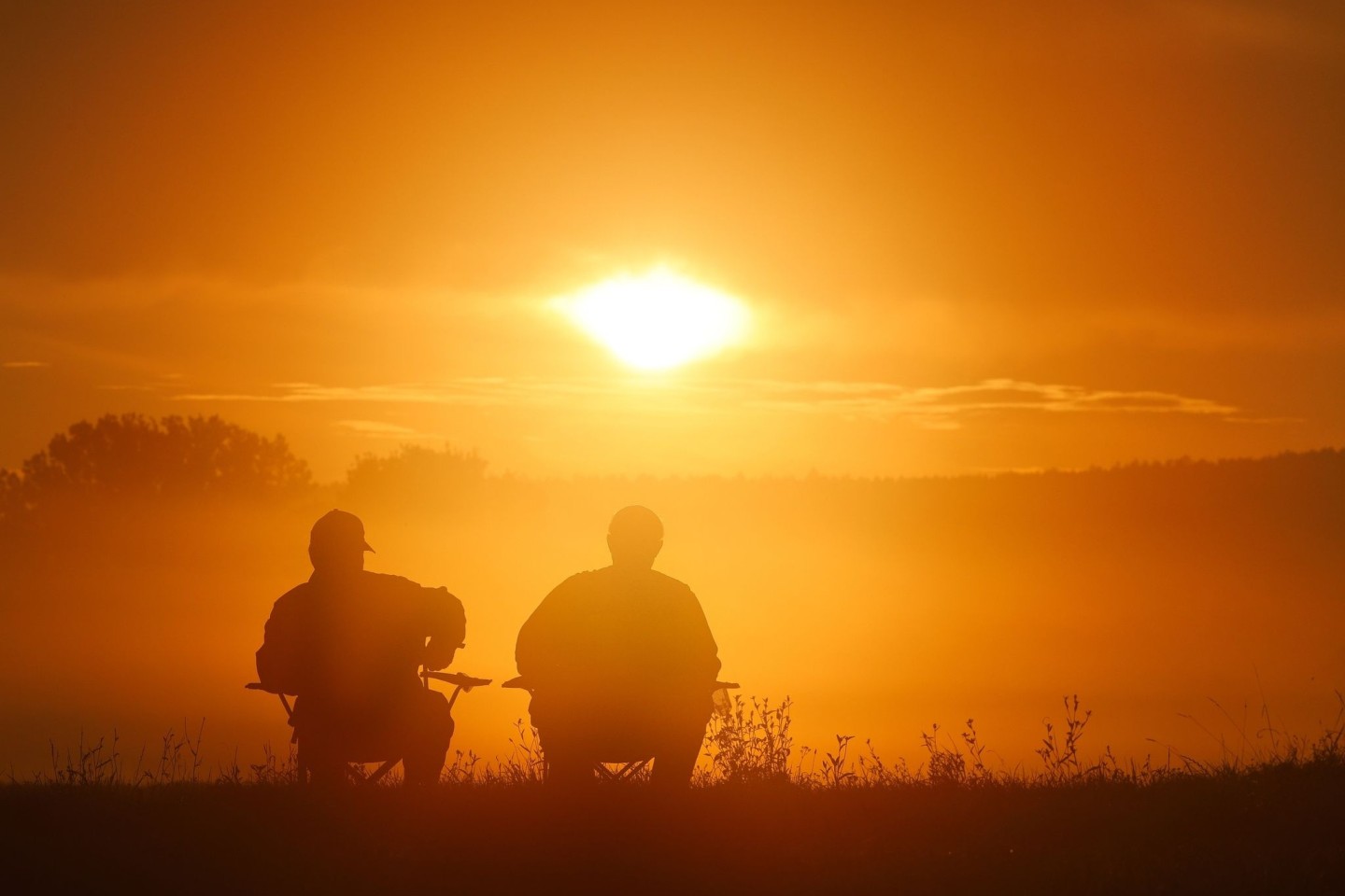 Zwei Angler sitzen auf Campingstühlen und schauen sich den Sonnenaufgang in Baden-Württemberg an.